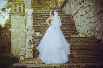 Beautiful bride walking near old castle before wedding ceremony