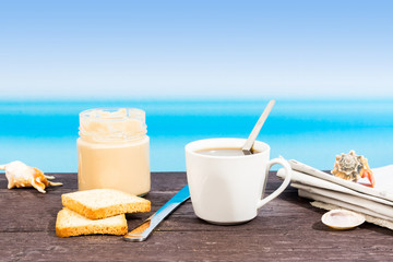 Tropical sea seen from the boat. Cream, coffee and newspaper on table. Breakfast in vacation