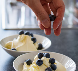 Hand, die Heidelbeeren über selbstgemachtes Eis streut
