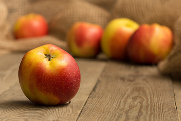 Close-up of a red and yellow apple on a wooden board with four more apples and hessian in the background