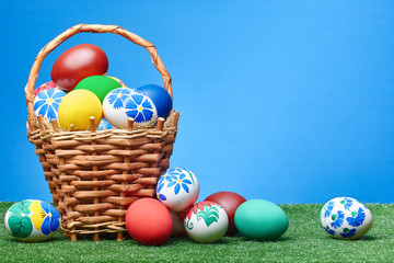 A wicker basket with Easter eggs stands on a lawn on a blue background