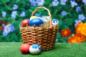 Wicker basket with Easter eggs against the background of summer flowers