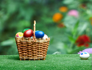 Wicker basket with Easter eggs against the background of summer flowers