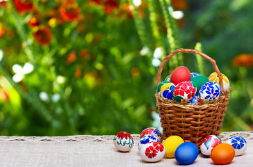 Wicker basket with Easter eggs against the background of summer flowers