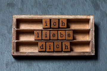 Ich liebe dich. I love you in German translation. Vintage box, wooden cubes phrase written with old style letters. Gray stone textured background. Close-up, up view, soft focus