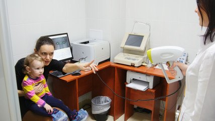 Optometrist checks child's eyesight - mother and child in ophthalmologist room