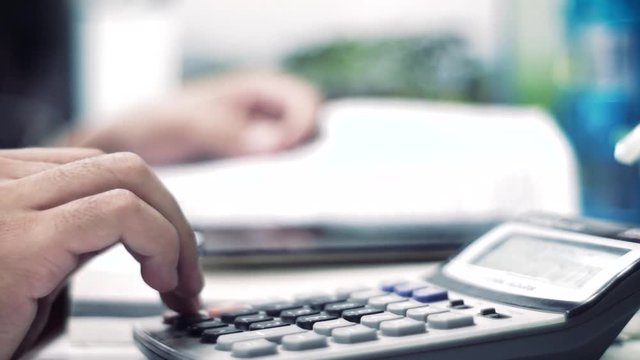 Men's hands typing on calculator and writing