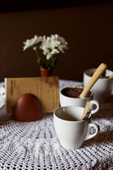 still life. White porcelain cups and a vase of flowers stand on a table with a white tablecloth in a brown cafe hall