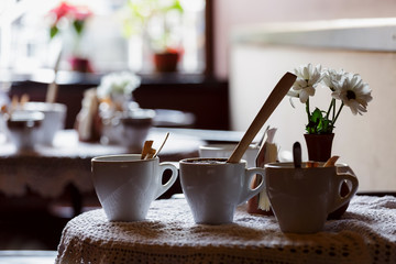 still life. White porcelain cups and a vase of flowers stand on a table with a white tablecloth in a brown cafe hall