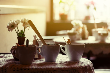 still life. White porcelain cups and a vase of flowers stand on a table with a white tablecloth in a brown cafe hall