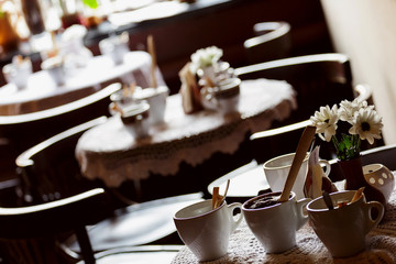 still life. White porcelain cups and a vase of flowers stand on a table with a white tablecloth in a brown cafe hall