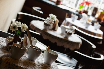still life. White porcelain cups and a vase of flowers stand on a table with a white tablecloth in a brown cafe hall