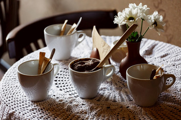 still life. White porcelain cups and a vase of flowers stand on a table with a white tablecloth in a brown cafe hall