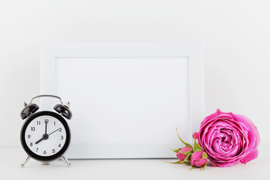 Mockup of picture frame decorated rose flower and alarm clock on white table with empty space for text and design your blogging.