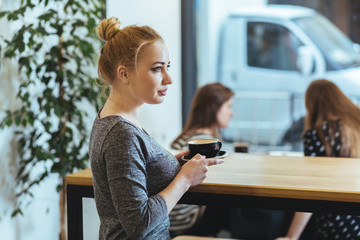Side view of blonde young woman drinking coffee in cafe