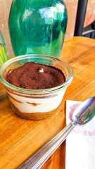 Tiramisu in glass cup on wooden surface.