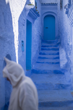 Man with a traditional dress is walking in the blue medina of Chefchaouen, Morocco.