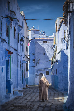 Man with a traditional dress is walking in the blue medina of Chefchaouen, Morocco.