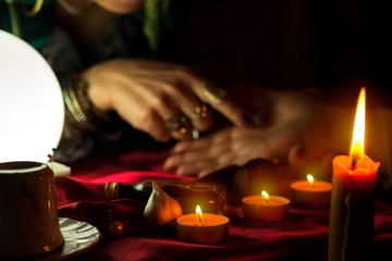 Fototapeta na wymiar Burning candles and woman who reads future from palm in the background