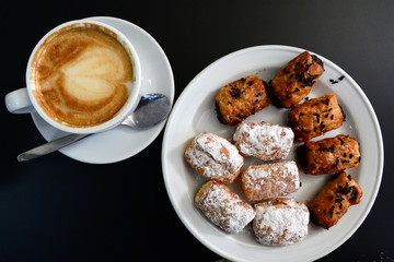 Cup of delicious foamy cappuccino with dessert on a black background.