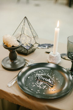 Wedding tableware with name card, stone candlestick with candle and other elements of festive table wedding centerpieces decorations.