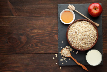 Bowl of oat flakes with honey, apple and milk on wooden background.