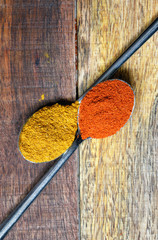Top view on a wooden rustic old table with two spoons of chili pepper and turmeric . Food background. Red and yellow colors.
