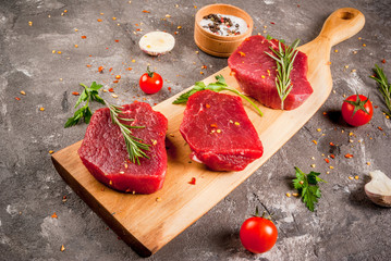 Fresh raw unprepared meat beef on a cutting board. With garlic, tomatoes, spices, herbs and salt. On a gray concrete table, copy space