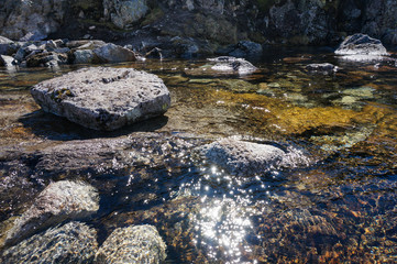 fast clean creek on the top of mountain with stones in bright day