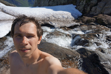 man making selfie topless on the top of mountain with creek on background after swimming in it