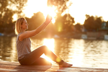Female making selfie by the river at sunset