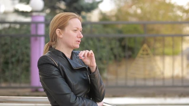 Sad woman without makeup nervously smokes in the street