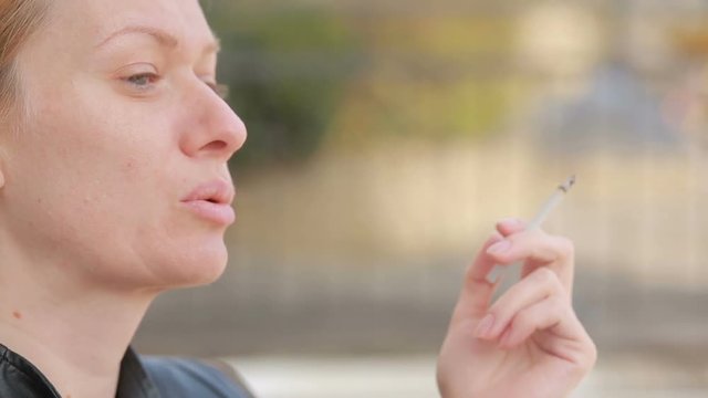 Sad woman without makeup nervously smokes in the street
