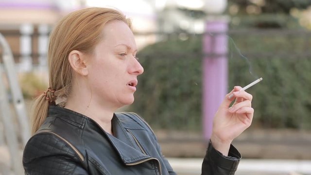 Sad woman without makeup nervously smokes in the street