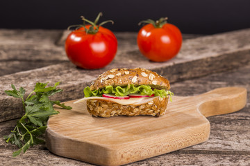 Healthy sandwich made with whole grain bread, lettuce, tomato, radish, cheese and roasted chicken slices.