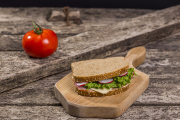Healthy sandwich made with whole grain bread, lettuce, tomato, radish, cheese and roasted chicken slices.