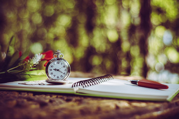pen, packet watch and rose  on the desk, open a blank white notebook on table