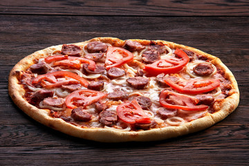Fresh pizza with tomatoes, cheese, onions and sausage on wooden table closeup