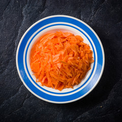 sliced carrots in a bowl on black stone background.