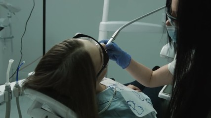 Female dentist drilling tooth of young female patient at the dentist cabinet.