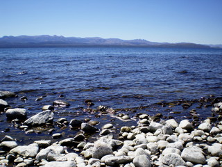 Blue lake with rocky coastline and mountain range background.