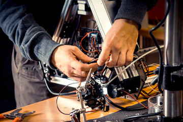 Two male masters work in the workshop with electronics, wires, 3d printer