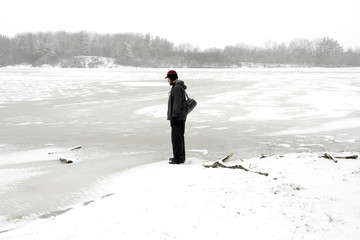 Rugged outdoors man stopping to look at a frozen lake  while on a winter hike