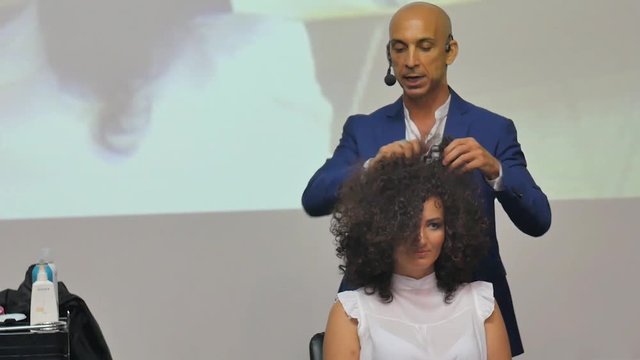 Hairdresser In Action. Barber makes a hair dryer dries hair curly brunette. Blonde in the cabin. Barber makes a hair dryer dries hair curly brunette in beauty salon