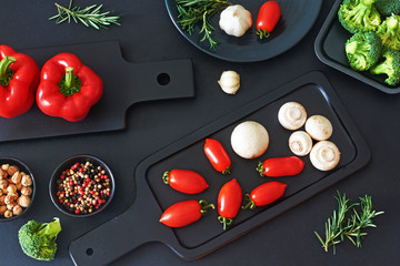 Stylish vegetarian dinner ingredients. Fresh vegetables, mushrooms and seasoning on a black background. Bell pepper, cherry tomato, champignon, broccoli. Top view.