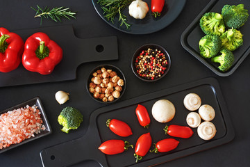 Stylish vegetarian meal ingredients. Fresh vegetables, mushrooms and seasoning on a black background. Bell pepper, cherry tomato, champignon, broccoli. Top view.
