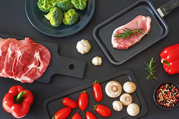 Thinly sliced beef and pork steak ready for preparation. Fresh vegetables and seasoning over black board. Stylish dinner ingredients. Top view.