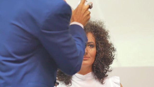 Hairdresser In Action. Barber makes a hair dryer dries hair curly brunette. Blonde in the cabin. Barber makes a hair dryer dries hair curly brunette in beauty salon