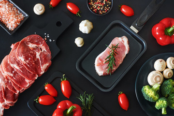 Grill or stir fry ingredients. Thinly sliced raw beef, raw pork steak in the pan with seasoning and fresh vegetables (bell pepper, broccoli, tomato, mushrooms) over black background. Top view.
