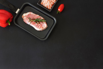 Raw pork or beef steak ready for frying or grill, bell pepper and cherry tomato over black board. Copy space, top view/